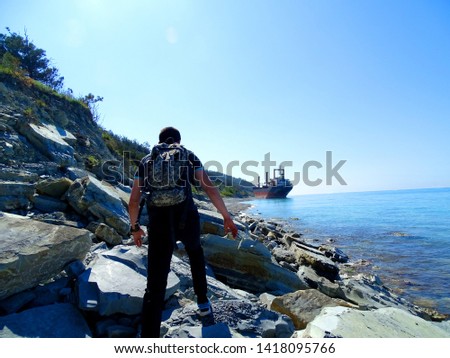 Unknown man walks over stones along the coastline. The man has a camouflage backpack