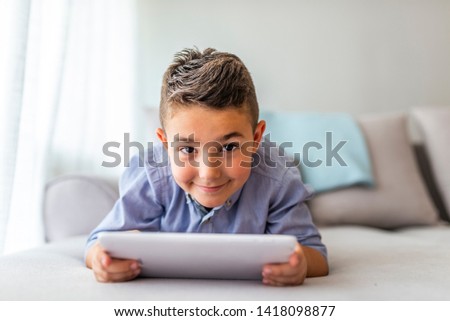 Boy playing with digital tablet. Little boy lying on the sofa and using digital tablet. Little boy with digital tablet sitting on sofa, on home interior background