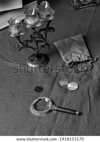 Black and white picture with the candles and the coins and a magnifier on the table