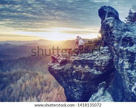 Photographer is taking pictures with camera in morning hills. Nature landscape photographer with photo equipment on rock. Silhouette of hiker woman