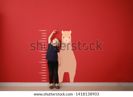 Surprised little boy measuring height near color wall