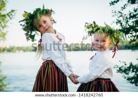 Light hair girls in Latvian traditional clothing posing on nature background. Preparing Ligo festival. Riga. Latvia Royalty-Free Stock Photo #1418242760