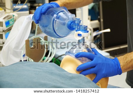 Doctor shows the use of a ventilation mask on a medical patient simulator in the operating room of a hospital                          Royalty-Free Stock Photo #1418257412