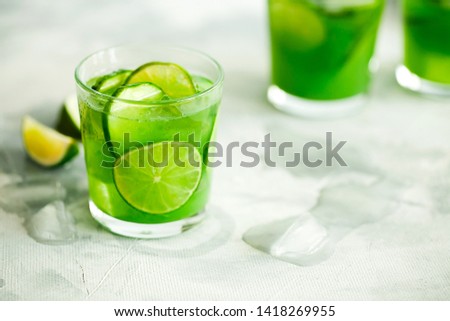 Homemade trendy iced matcha green tea or lemonade with cucumber and lime in a glass on light gray background with copy space for text.Healthy cold vegan beverage for hot summer day.Super food drink