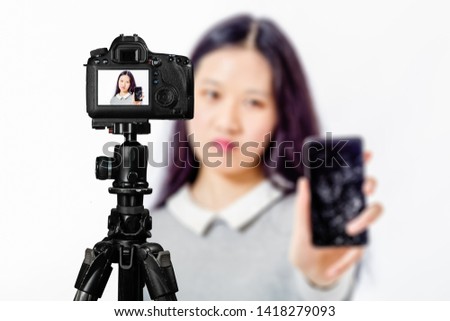 Focus on live view on camera on tripod, teenage girl  holds cracked phone image on back screen with blurred scene in background. Teenage vlogger livestreaming show concept