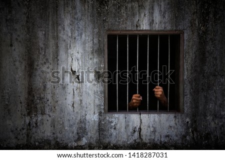 Hands of the prisoner on rusty bar of window and old grungy prison cell wall Royalty-Free Stock Photo #1418287031