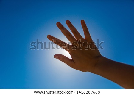 hand covers the sun against the blue sky