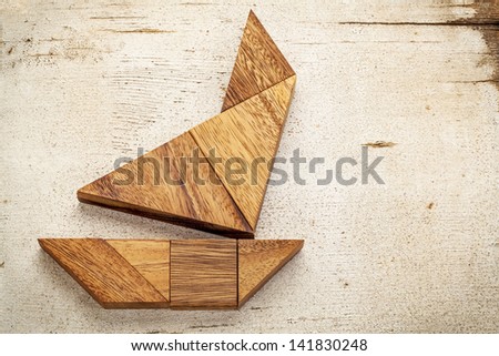 abstract picture of a sailing boat built from seven tangram wooden pieces over a rustic white painted barn wood