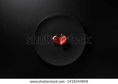 One sliced strawberry served in black plate on moody black background. Top view. Healthy diet concept. 