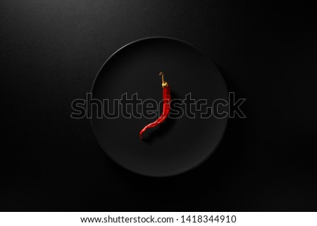 One dry red hot chili pepper served in black plate on black background. Top view  Royalty-Free Stock Photo #1418344910