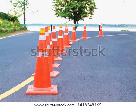 Many orange warning cones on curved roads On the asphalt road background and green trees with a copy area. Selective focus.