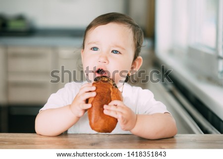 a little girl in the kitchen during the day eating a bun with poppy seeds is very appetizing and greedy