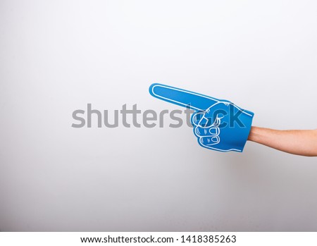 Handsome fan hand glove with foam finger, pointing away over white wall background Royalty-Free Stock Photo #1418385263