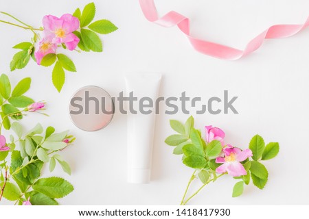 Flat lay composition with cosmetic products, mockup white tubes and pink flower on a white background