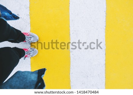 Women's legs in jeans and sneakers on a white and yellow pedestrian crossing top view