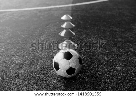 black and white iamge of cone marker and football are soccer training equipment on green artificial turf. Soccer Academy.