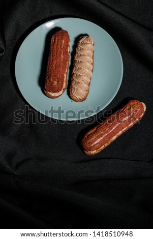 two red eclairs on a blue saucer and one on a black background