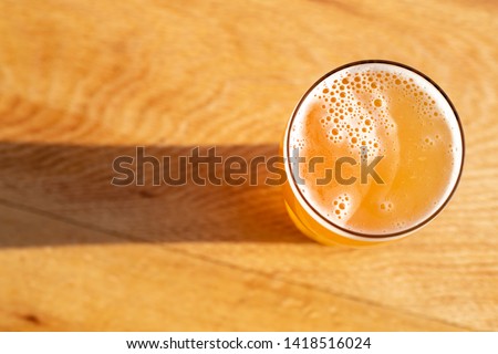 Flat lay of a pint of golden pale ale beer casting a shadow on a wood table, with space for text on the left 