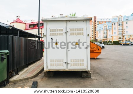 Grey electric Transformer room building with white doors and yellow hazard signs in the city on blue sky background