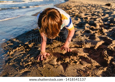 Child kneeling tired after running on the beach during his holidays.