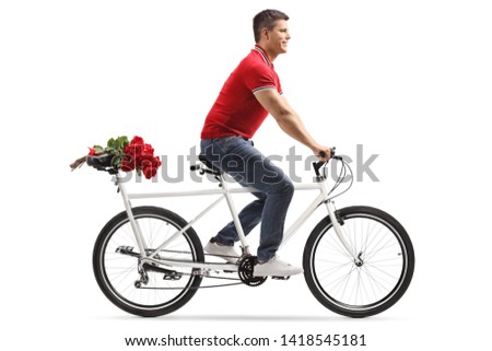 Full length shot of a young cheerful man riding a tandem bicycle and carrying red roses on the back seat isolated on white background