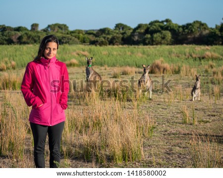 Young girl with a pink jacket standing in front of 3 curious kangaroos