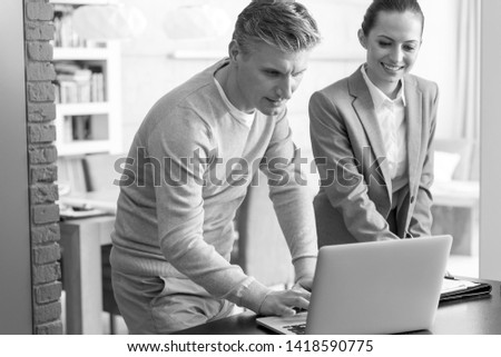 Black and White photo of Mature man and saleswoman discussing over laptop table in apartment