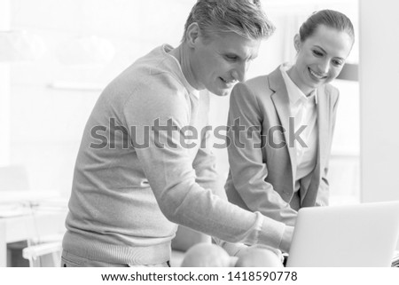 Black and White photo of Smiling mature man and saleswoman discussing over laptop in apartment