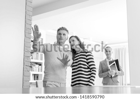 Black and White photo of Confident saleswoman looking at couple discussing in apartment
