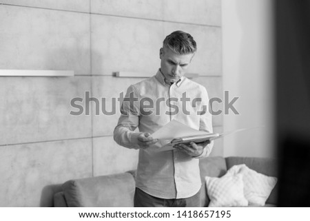 Black and White photo of Mature man reading document while standing against wall at home