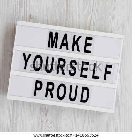 Light box with text 'Make yourself proud' on a white wooden background, top view. Flat lay, overhead, from above. 