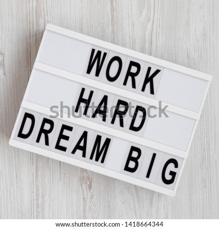 'Work hard dream big' words on a modern board on a white wooden background, top view. Flat lay, overhead, from above. 
