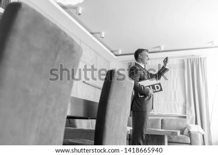 Black and White photo of Confident mature male realtor holding sold placard while photographing at home