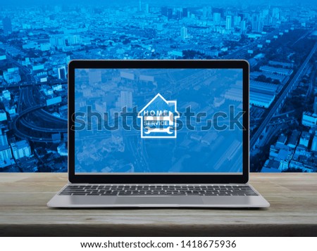 Hammer and wrench with house flat icon with modern laptop computer on wooden table over city tower, street, expressway and skyscraper, Business home service online concept
