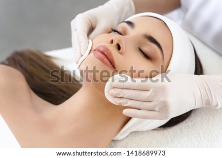 Close up of hands of skillful beautician cleaning and touching female face with cotton pad or sponge. The woman is lying and relaxing. Her eyes are closed with pleasure Royalty-Free Stock Photo #1418689973