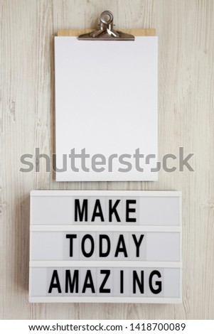 'Make today amazing' words on a modern board, clipboard with blank sheet of paper on a white wooden surface. From above, overhead, flat lay, top view.