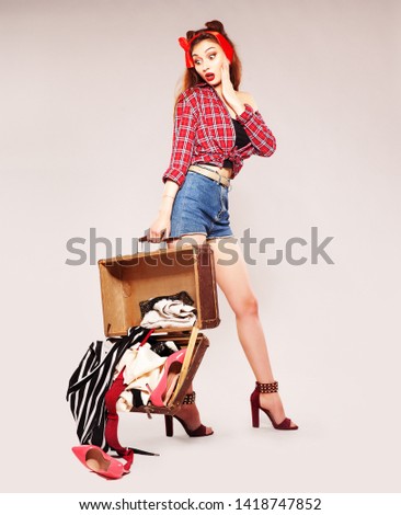 beautiful happy girl in pin-up style in shorts and a plaid shirt with a suitcase in her hands.Vintage photography.Wonderful traveler. Vacation season.