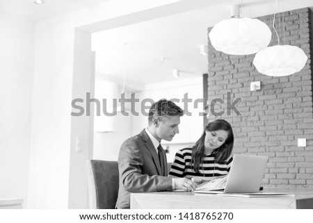 Black and White photo of Mature male realtor explaining document to female buyer at table in apartment