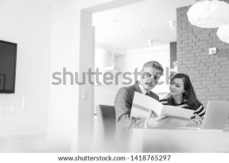 Black and White photo of Mature male realtor and female buyer reading document while sitting at table in apartment
