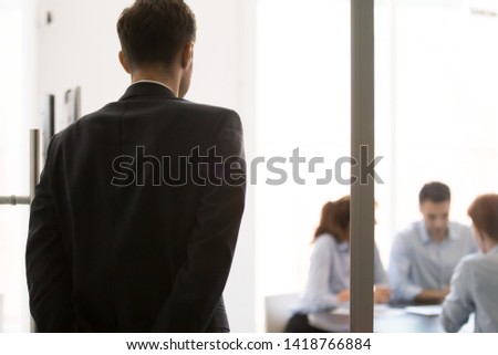 Rear view nervous man standing near glass door waiting looking at participants sitting at desk at business meeting. Lack self-confidence, public speaking fear, stressed applicant before job interview Royalty-Free Stock Photo #1418766884