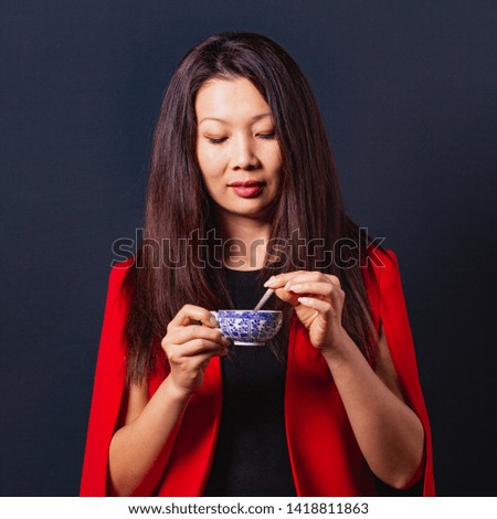 Beautiful asian business woman in a elegant red suit with a cup of coffee on a dark blue background, front view.