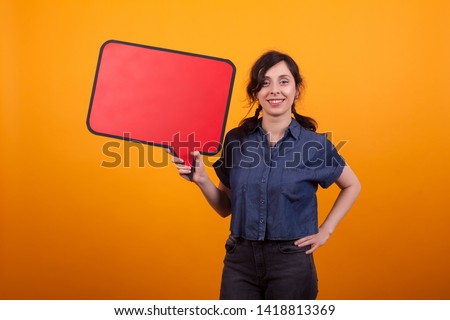 Portrait of young woman holding red thought bubble over yellow background in studio. Cheerful woman with banner in her hand.