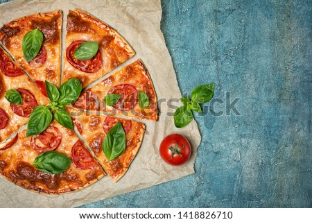 Top view of round pizza margarita with tomato, cheese and basil leaves for vegetarians on blue concrete background with copy space