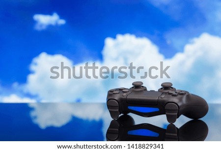 Modern black gamepad against the blue sky. Joystick black color on a smooth reflective table. Gaming concept