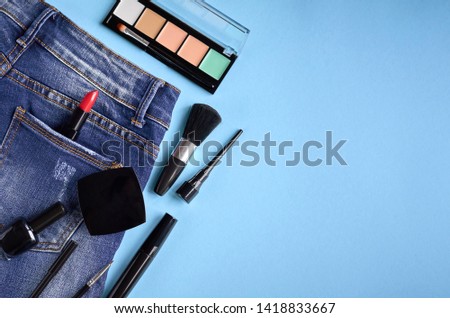 Different makeup products composition with jeans on blue background, flat lay and top view photo