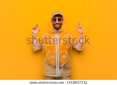 Young man wearing a rain coat crossing fingers for having luck