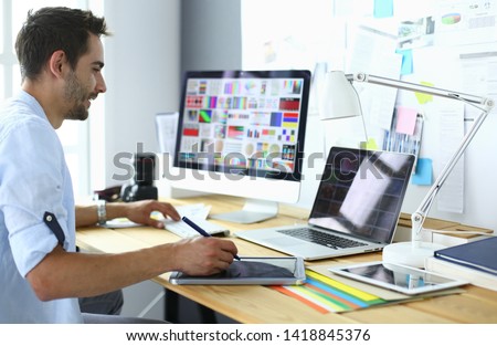 Portrait of young designer sitting at graphic studio in front of laptop and computer while working online. Royalty-Free Stock Photo #1418845376