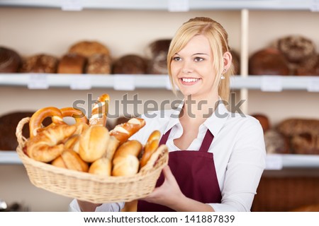 Happy young waitress giving breadbasket while looking away in cafe