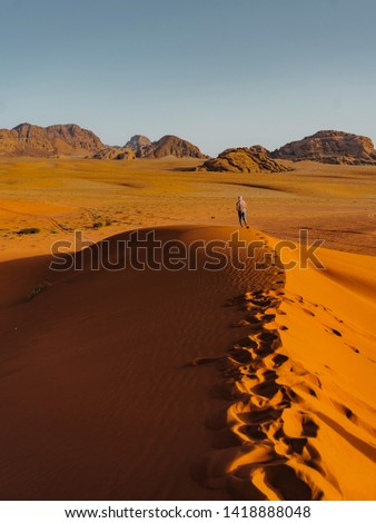 
Crazy man running overlooking the red sand desert as seen with a cloudy golden sunset in Wadi Rum, Jordan. Fearless hiker he lost in the desert. Close to the horizon. Pure nature landscape