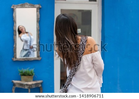Beautiful woman on white dress looking at herself on a mirror at the colorful streets of the colonial walled city of Cartagena de Indias
